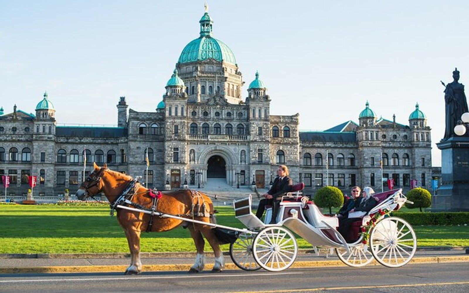 A Victoria horse carriage tour travels in front of the Parliament Buildings.