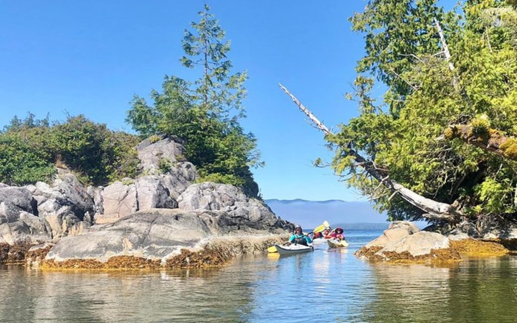 a group paddles through a narrow pass on a kaying tour of barkley sound on vancouver island