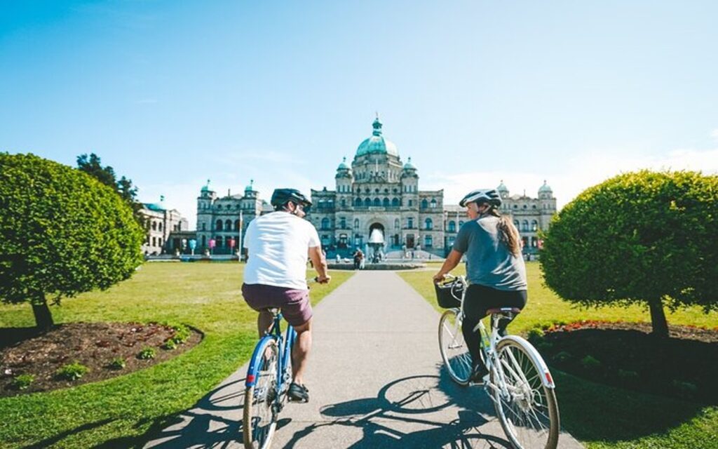 a couple passes the parliament buildings on a bike tour of victoria, bc