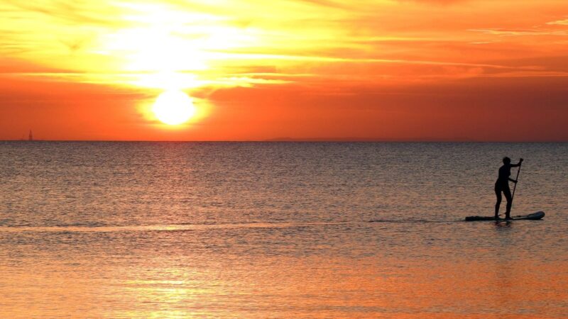 a man enjoys paddleboarding victoria at sunset.