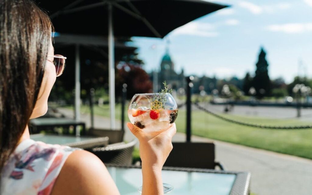 A woman sips her drink overlooking the Inner Harbour at the Fairmont Hotel's Veranda, one of the best patios in Victoria, BC.